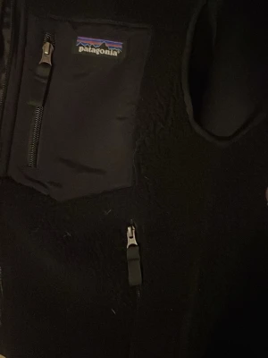 Svart fleeceväst från Patagonia XS - Svart fleecejacka från Patagonia i storlek XS. Jackan har flera praktiska fickor med dragkedja och klassisk Patagonia-logga på bröstet. Materialet är mjuk fleece och jackan har en sportig look med detaljer i syntet. Perfekt för dig som gillar outdoor och street. Startpris 600, kan sänka bara att meddela!!!