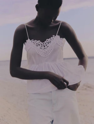 Vit spetsdetaljerad linnetopp - Supersöt vit linnetopp med tunna axelband och spetsdetaljer vid halsringningen. Toppen har en luftig, volangig nederdel som ger en romantisk vibe. Perfekt för varma dagar och att styla med jeans eller kjol.