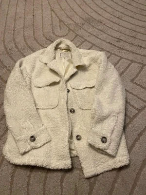 Vit teddyjacka från Samsa - Supermjuk och fluffig vit teddyjacka från samsamed stora bröstfickor och knappar framtill. Jackan har klassisk krage och långa ärmar med knappdetaljer vid ärmslut. Perfekt för dig som vill ha en mysig och trendig look. Strl 146/152 så passar mig xs/s