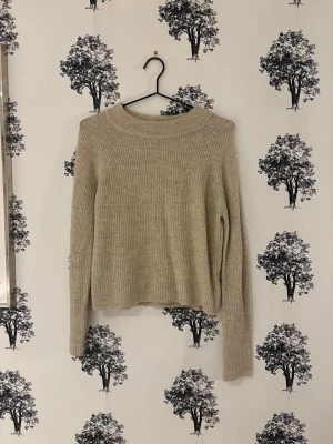 Beige ribbad stickad tröja från Pieces - Mysig beige stickad tröja med ribbad struktur och rund hals. Tröjan har lång ärm och en något croppad passform som ger en avslappnad vibe. Perfekt att matcha med jeans eller kjol för en enkel men snygg look.