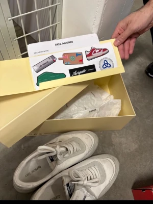 Vita sneakers från Axel Arigato - Snygga vita sneakers från Axel Arigato med klassisk låg siluett. Skorna har snörning, rund tå och detaljer i både skinn och mocka. Perfekta för dig som gillar stilrena och trendiga sneakers med minimalistisk design.