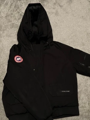 Svart dunjacka från Canada Goose - Säljer en svart Canda Goose dunjacka med huva Perfekt för kyliga vinterdagar och riktigt snygg streetstil. Storlek S