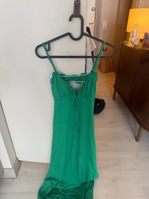 Grön långklänning med snörning - Snygg grön långklänning med smala axelband och snörning framtill. Klänningen har en feminin volangdetalj vid bysten och är tillverkad i ett mjukt, lätt tyg som faller fint. Perfekt för varma dagar och somriga tillfällen.