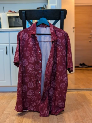 Kortärmad skjorta – vinröd/blommig – SHEIN – stl L - Säljer en kortärmad skjorta från SHEIN i vinröd färg med blommigt mönster. Använd några gånger men i fint skick. 🔸 Storlek: L (upplevs som lite större i passformen) 🔸 Lätt och luftig – perfekt till sommaren 🔸 Knäppning framtill 🔸 Inga hål eller fläckar Pris: 100 kr Kan skickas mot frakt eller hämtas upp enligt överenskommelse. Hör av dig vid intresse!