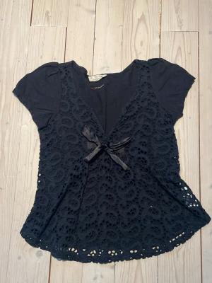 Svart/mörkblå blus - Säljer en blus från odd Molly med korta puffärmar och v-ringning. Framsidan har ett detaljerat spetsmönster och ett band som går att knyta roset med. Blusen är tillverkad i bomull och har en mjuk, loose passform som ger en chill vibe.