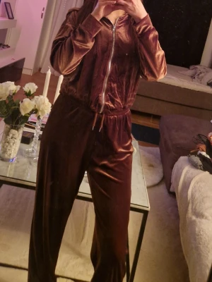 Brun velour loungewear-set - Mysigt loungewear-set i brun velour med dragkedja framtill och resår i midjan. Setet består av en långärmad ziptröja och matchande byxor med avslappnad passform och dragsko. Perfekt för chill dagar hemma.
