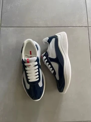 Blåvita sneakers med mesh och lackdetaljer - Snygga sneakers i marinblått och vitt med meshpaneler och blanka lackdetaljer. Skorna har vit sula, rund tå och klassisk snörning. Perfekta för dig som gillar sportig och modern stil.