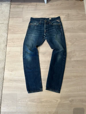 Replay jeans blå - Klassiska Replay jeans i mörkblå tvätt med raka ben och femficksmodell. Jeansen har en tidlös look med kontrastsömmar och knappgylf. Perfekta för dig som gillar en avslappnad och ikonisk stil.