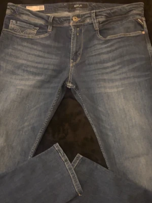 Replay blå jeans med raka ben - Snygga blå jeans från Replay med klassisk femficksdesign och raka ben. Jeansen har subtila slitningar framtill och ljusare partier för en cool look. Märkespatch bak i midjan och detaljerade bakfickor. Perfekta för dig som gillar stilrena jeans.