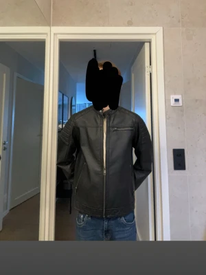 Svart skinnjacka från Jack & Jones - Säljer för den är för liten men tvär fet och helt ny storlek 152 snygg svart skinnjacka från Jack & Jones med ståkrage och dragkedja framtill. Jackan har diskreta sömdetaljer på axlarna och en bröstficka med dragkedja. Perfekt för dig som vill ha en stilren och klassisk look.