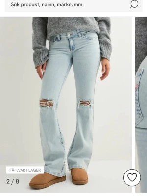 Nelly ljusblå stitch jeans (s32short) - Säljer ett par ljusblå bootcut jeans med slitna hål över knäna. Jeansen är stretchiga och i storlek 32 short