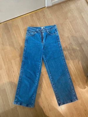 Blå raka jeans från Dagmar - Säljer ett par klassiska blå jeans från Dagmar med raka ben och hög midja. Jeansen har  fickor, bälteshällor och en tydlig dragkedja framtill. Perfekta för en avslappnad och trendig look.