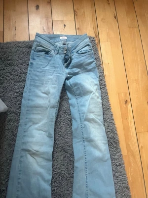 Ljusblå bootcut jeans  - Säljer ett par ljusblå bootcut jeans med snygga rosa broderade sömmar på bakfickorna. Jeansen har låg midja. Storlek 34/short endast använda ett fåtal gånger