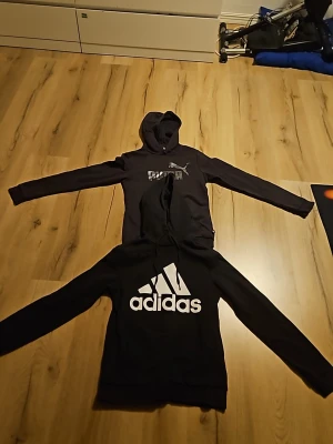 Svart Adidas hoodie med stor logga - Säljer 2 hoodies för 200. en svart hoodie från Adidas med stor vit logga och text på bröstet, i stl UK xs 4-6. Och en puma hoodie med vit text på bröstet, i stl UK 13-14y sitter som stl 146-152. Klassisk modell med huva och långa ärmar. Perfekt för dig som gillar sportig och avslappnad stil. Är tvätade en hel del så den är inte lika mjuk. En för 120kr två för 200kr. skriv om ni har frågor