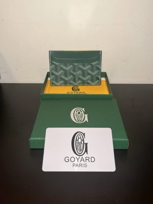 Grön Goy4ard plånbok med mönster - Snygg grön plånbok från Goy4ard med ikoniskt vitt och grått grafiskt mönster. Plånboken är kompakt och har flera fack för kort. Tillverkad i exklusivt skinn och levereras med original ask och dustbag. Perfekt för dig som vill ha något stilrent och lyxigt.