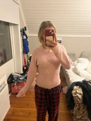 Ljusrosa stickad tröja - Mysig ljusrosa stickad tröja med rund halsringning och långa ärmar. Tröjan har en figurnära passform och ribbstickad struktur som ger en trendig och bekväm look. Perfekt att matcha med jeans eller kjol för en avslappnad stil. Omsydd.