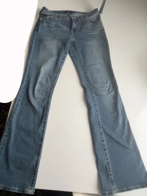 Blå bootcut jeans med utsvängda ben / true religion från nelly  - Säljer ett par ljusblå bootcut jeans med riktigt utsvängda ben. Klassisk femficksmodell och normal midja. Perfekta för dig som gillar retrovibbar och vill ha ett par jeans som sticker ut sopar golvet med sin coola siluett.