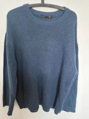 Blå stickad tröja från 157 - Mysig blå stickad tröja från 157 med rund halsringning och ribbade muddar. Tröjan har en enkel och avslappnad passform, perfekt för lager på lager. Materialet känns mjukt och behagligt mot huden.