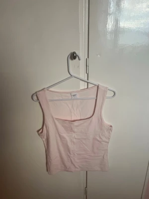 Ljusrosa ärmlös linnetopp - Söt ljusrosa linnetopp med breda axelband och fyrkantig ringning. Toppen är croppad och har en enkel, stilren design som passar perfekt till jeans eller kjol. Tillverkad i mjukt bomullsmaterial för en bekväm känsla.