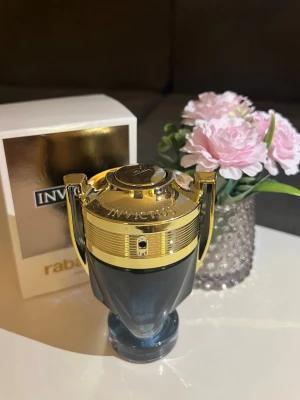 Paco Rabanne Invictus parfym - Snygg parfymflaska från Paco Rabanne i modellen Invictus. Flaskan har en unik troféform med guldfärgade detaljer och mörkgrått glas. Kommer med originalförpackning i guld och vitt. Perfekt för dig som gillar exklusiva och moderna dofter.