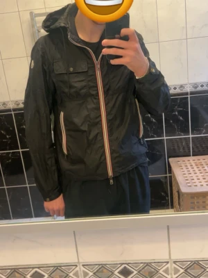 Svart vindjacka från moncler - Snygg svart vindjacka med huva och färgglada detaljer på dragkedjorna. Jackan från moncler är perfekt till våren!