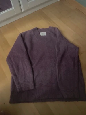 Lila stickad tröja från Zara - Mysig lila stickad tröja från Zara med v-ringning och breda ribbade muddar vid ärmslut och nederkant. Perfekt för lager-på-lager och enkel att matcha med jeans eller kjol. Materialet är mjukt och skönt mot huden. Det står storlek 152 men skulle säga att det passar bra som xs/s