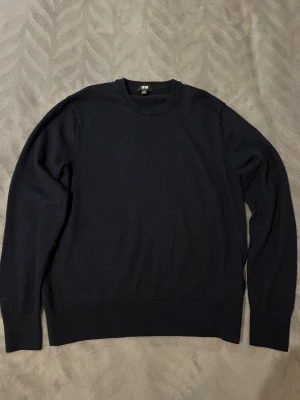 Svart stickad tröja från Uniqlo - Klassisk svart stickad tröja från Uniqlo med rund halsringning och långa ärmar. Tröjan har ribbade muddar vid ärmslut och nederkant, vilket ger en snygg och enkel look. Perfekt basplagg i garderoben för dig som gillar stilrena outfits.