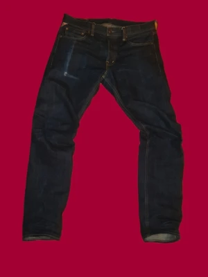 Ralph Lauren jeans - Säljer ett par mörkblå jeans från Denim & Supply Ralph Lauren. Klassisk femficksmodell med snygga kontrastsömmar och en liten detalj med amerikansk flagga vid fickan. Jeansen har rak passform och är tillverkade i slitstarkt bomullsdenim.