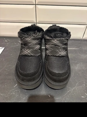 UGGs LOW MEL - Säljer ett par svarta sneakers från UGG med grova snören i svartvitt mönster och mjukt, fluffigt foder på insidan. Ovandelen är i textil och mocka, och sulan är platt. Perfekta för kyligare dagar och riktigt sköna att ha på sig. Billigare pris vid snabb affär✅