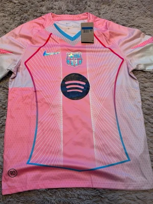 Rosa FC Barcelona tröja - Den är storlek M, men sitter lite slim så den kan passa S.  Säljer en riktigt snygg rosa FC Barcelona matchtröja från Nike med holografiska detaljer, klubbmärke och Spotify-logga på bröstet. Tröjan har V-ringning med blå kant och är tillverkad i ett lätt, ventilerande material perfekt för träning eller match.