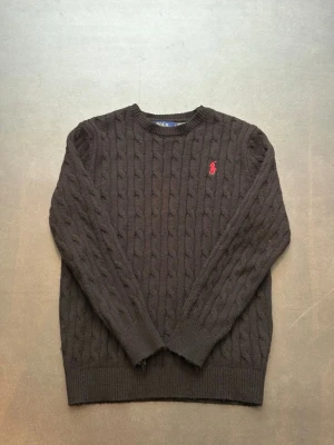  kabelstickad tröja Polo Ralph Lauren - Svart kabelstickat tröja från Ralph Lauren nytt skick köpte ny men gilla inte. Sitter lite tajt och lite kort jag är 175cm väger 55kg. Frågor hör av er.