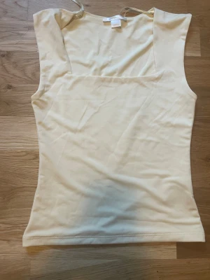 Ljusgul ärmlös linnetopp från Gina Tricot - Säljer en stilren ljusgul linnetopp från Gina Tricot. Toppen är ärmlös med breda axelband och har en rak, något croppad passform.  Perfekt till sommaren och enkel att matcha med olika outfits.