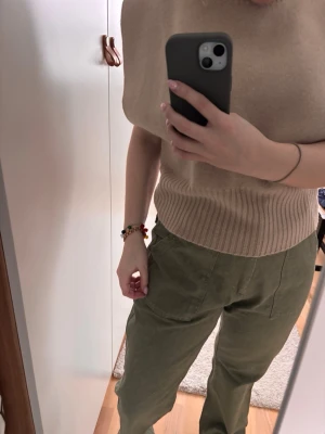 Beige stickad topp från Zara - Säljer en beige stickad topp från Zara med bred ribbad kant nertill och vid ärm. Toppen har en enkel, rund halsringning och är ärmlös med en loose fit. Perfekt att styla med jeans eller kostymbyxor för en clean look. Nypris 399kr