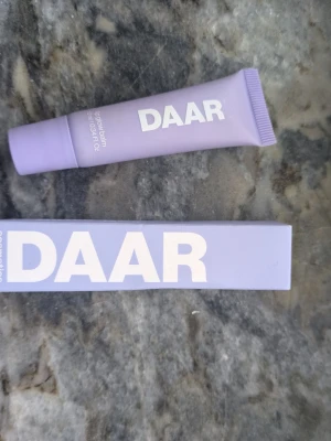 DAAR Purple Vanilla Lip Balm - Läppbalsam från DAAR i doften Purple Vanilla + Sweet Strawberry. Kommer i en lila tub med vit text och har en mjuk applikator. Ger en hint av rosa färg på läpparna och innehåller bland annat sheasmör, solrosolja och ginsengextrakt. Tuben rymmer 10 ml. Endast testad på handen, nypris 219