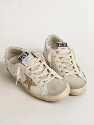 Golden Goose sneakers med glitterstjärna - Snygga vita sneakers från Golden Goose med silvriga detaljer och en glittrig stjärna på sidan. Skorna har snörning, platt sula och inslag av mocka vid tån och hälen. Perfekta för dig som vill sticka ut med en cool och trendig look.