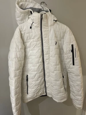 jacka från Peak Performance - Säljer en vit pufferjacka från Peak Performance med quiltat mönster och huva.