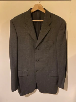 Prada kostym - Säljer en kostym från Prada i grå färg. Kavajen är i fin kvalitet och bra skick men är lite nopprig på ryggen (visas på bilden). Kostym byxorna är slitna och uppsydda men det går lätt att förlänga dom igen.