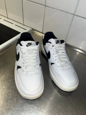Nike Air Force 1 svartvita sneakers - Nike Air Force 1 sneakers i svart och vitt med klassisk låg siluett. Skorna har vit ovandel i skinn med svarta detaljer och Nike swoosh på sidorna. Tjock vit sula med svart yttersula och vadderad krage för extra komfort. Perfekta för dig som gillar stilrena och tidlösa sneakers. ( andvända en gång) ! 
