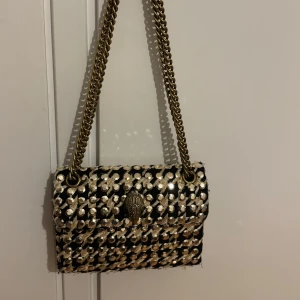 Svart och guld axelväska med paljetter - Kurt Geiger väska i svart tyg med guldiga paljetter och broderier. Orginalpriset är 2000kr men säljer för endast 850kr pågrund av defekter, (tyget har slitits lite på botten) 💞