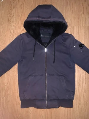 Mörkblå Moose Knuckles Classic Bunny hoodiejacka - Säljer en Mörkblå Classic Bunny från Moose Knuckles i storlek XS. Jackan har dragkedja, huva med mjuk fuskpäls och quiltat innerfoder. Snygg logga på ärmen och två stora fickor framtill. Perfekt för kalla dagar och går även att ta ut pälsen för lite varmare dagar. I bra skick finns tecken på användning såsom att den har blivit lite solblekt samt att fickorna har minimala slitningar, ingenting som syns eller påverkar funktionen helt enkelt. Storlek XS men passar en S bättre!