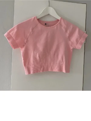 Ljusrosa croppad topp - Säljer en ljusrosa croppad topp med korta ärmar och rund hals. Toppen är ribbad nedtill och har en enkel, stilren design. 