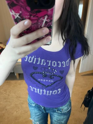 Lila t-shirt med pärldetaljer - Säljer en lila t-shirt från Nicpai med coolt tryck och pärldetaljer i form av ett hjärta på bröstet. T-shirten har korta ärmar och rund halsringning. Materialet känns mjukt och stretchigt, perfekt för en avslappnad look.