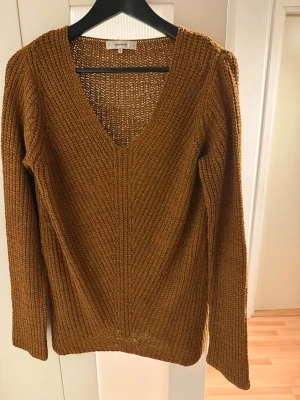 Brun stickad tröja från Soyaconcept - Mysig brun stickad tröja från Soyaconcept i storlek S. Tröjan har en djup v-ringning och långärmad passform. Perfekt för lager på lager under höst och vinter. Grovstickad struktur som ger en avslappnad och trendig look.