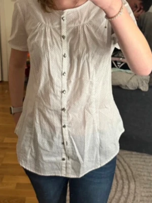 Vit prickig skjorta från Esprit - Snygg vit skjorta från Esprit med bruna prickar och korta ärmar. Modellen har rundad hals, knappar framtill och två dekorativa knappar på ärmsluten. Skjortan är tillverkad i mjuk bomull och har en loose passform som ger en chill vibe.