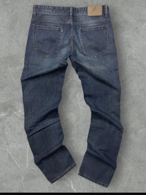 Levi's y2k mörkblå jeans straight fit - Klassiska Levi's 501 jeans i mörkblå tvätt med raka ben och femficksmodell. Jeansen har en snygg slitning, bruna kontrastsömmar och läderpatch bak i midjan. Tillverkade i robust bomullsdenim och har knappgylf framtill.