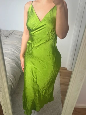 Grön långklänning från Zara - Säljer en snygg grön långklänning från Zara med omlott-v-ringning och tunna axelband. Klänningen har en figurnära passform och är gjord i ett glansigt, silkigt material som ger en lyxig känsla. Perfekt för dig som vill sticka ut med färg och stil 💚