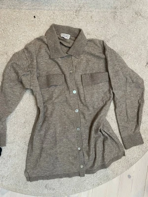 Beige kofta från & Other Stories - Säljer en beige kofta från & Other Stories med klassisk krage, långa ärmar och knappar framtill. Den är fläckig längst ner men går nog bort i tvätten. I ull! Säg till om du vill ha fler bilder eller vill diskutera pris💕. 