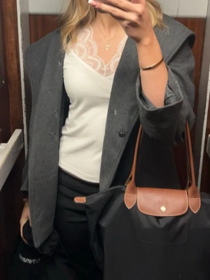 Grå kappa med huva och bälte - Säljer en snygg grå kappa med stor huva och knytskärp i midjan. Jackan har en loose passform och är tillverkad i ett mjukt ull-liknande material. Perfekt för dig som vill ha en stilren och enkel look med extra edge tack vare huvan.