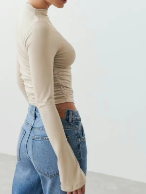 Beige långärmad rynkad topp - Beige, croppad långärmad topp med rynkade sidor. Den är från Gina Tricots ”Soft touch” serie. Slits vid ärmsluten. Väldigt lite använd, nyskick.