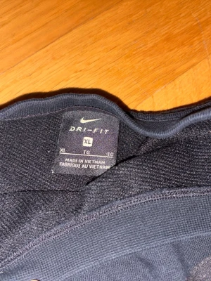 Svart Nike Dri-Fit sweatshirt - Säljer en svart Nike Dri-Fit sweatshirt i nikes barnstorlek xl, skulle säga att det är som s i normal storlek! Tröjan har en stor svart Swoosh-logga på bröstet och är gjord i ett mjukt funktionsmaterial som andas. Perfekt för dig som gillar sportig och clean stil. Glittrigt märke 